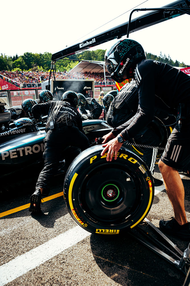 Los mecánicos del equipo Mercedes-AMG PETRONAS Formula One Team realizan una parada en boxes. Uno de los integrantes prepara un neumático Pirelli mientras los demás trabajan sobre el auto. El logo de Einhell se ve en el equipamiento por encima del vehículo.