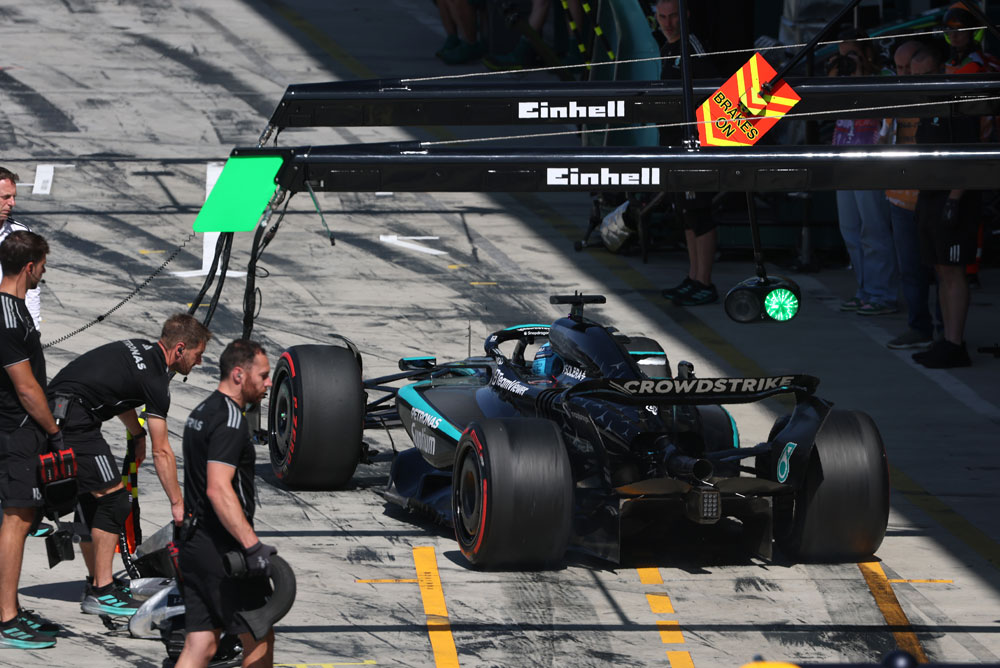Un auto del equipo Mercedes-AMG PETRONAS Formula One se encuentra en la calle de boxes durante una detención. Varios miembros del equipo rodean el auto. El logo de Einhell es visible sobre el área de boxes.