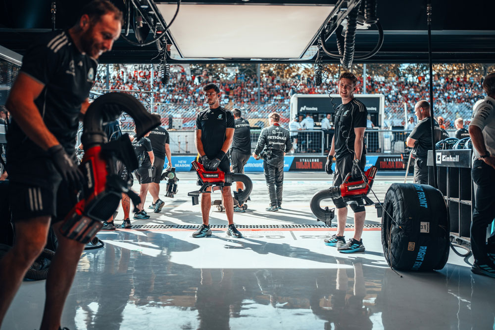 Los mecánicos del equipo Mercedes-AMG PETRONAS Formula One Team se preparan en el taller con sopladoras inalámbricas Einhell antes de una detención en boxes. Al fondo, las tribunas están llenas de fanáticos.