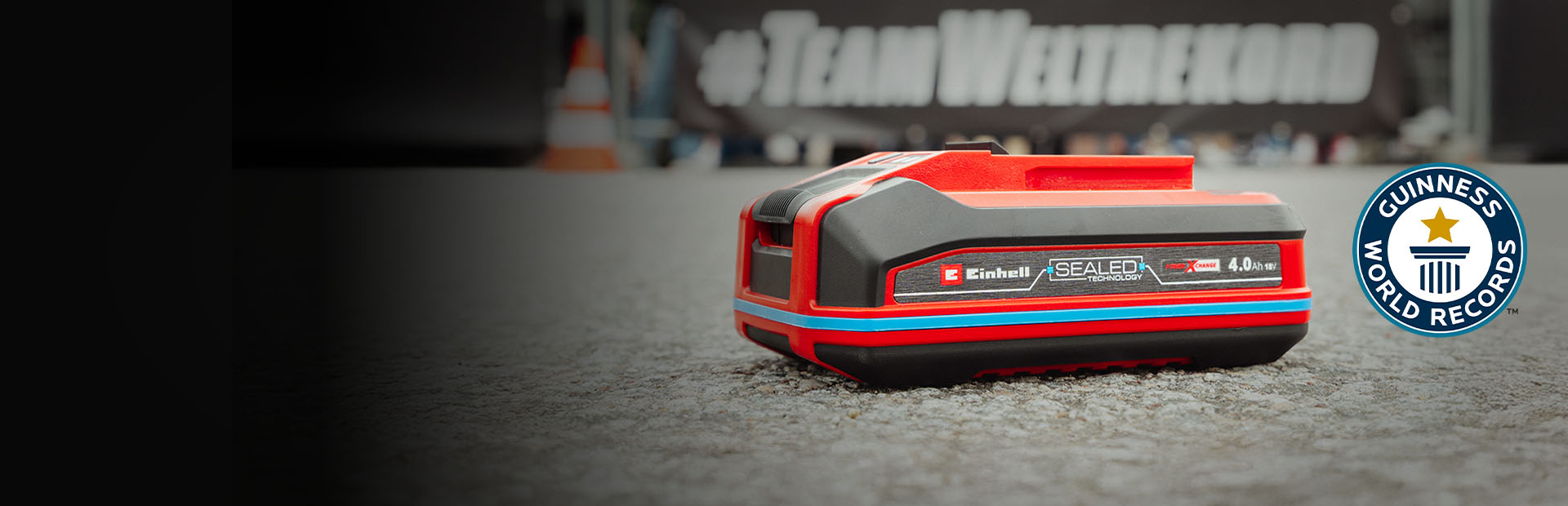 Batería Einhell SEALED Power X-Change 4.0 Ah sobre asfalto, con el logo de Guinness World Records "Record Holder" a la derecha.