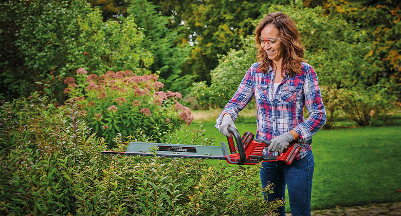 A woman is trimming a bush with an Einhell hedge trimmer