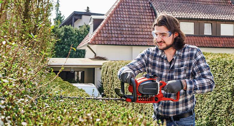 man cutting hedge with petrol hedge trimmer