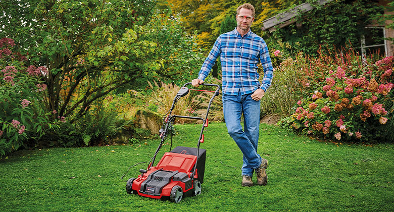 A man standing in the garden next to his corded scarifier.