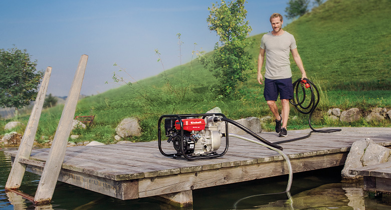  A man connecting a petrol water pump on a platform above a pond.