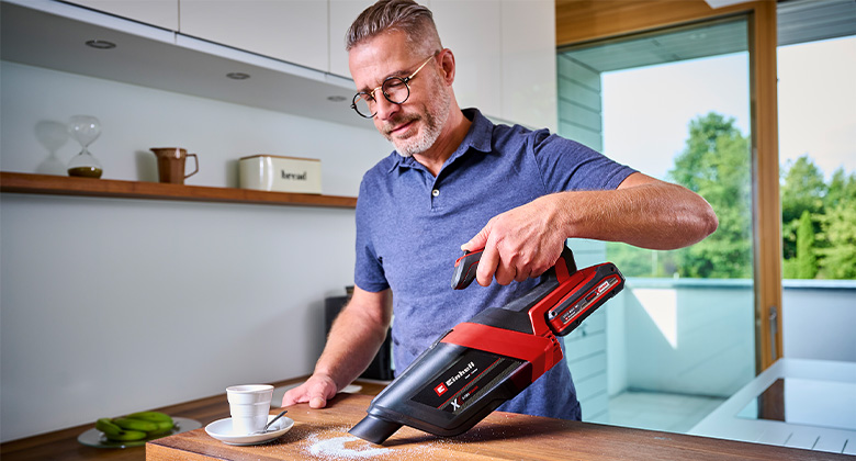 Man uses the Einhell cordless handheld vacuum to suck sugar from the kitchen surface